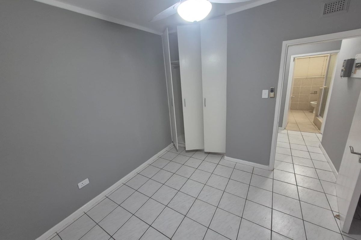 A vacant bedroom featuring tiled flooring, built-in cupboards, a ceiling fan, and direct access to an en-suite bathroom.