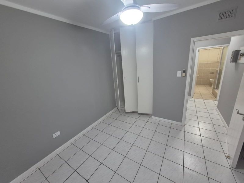 A vacant bedroom featuring tiled flooring, built-in cupboards, a ceiling fan, and direct access to an en-suite bathroom.