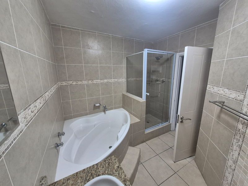 A functional bathroom featuring a built-in corner bathtub, a separate glass-enclosed shower, and neutral wall and floor tiling.