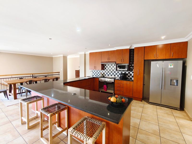 Spacious open-plan kitchen featuring wooden cabinetry, granite countertops, a central island, and tiled flooring, seamlessly flowing into the adjacent dining area.