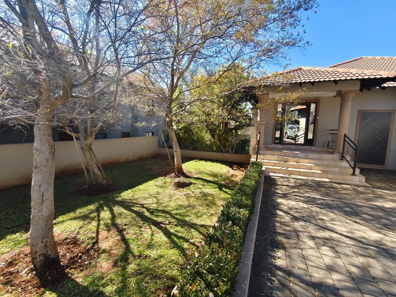 Front view of the property featuring a paved driveway, landscaped garden, and tiled entrance steps leading to the main doorway.
