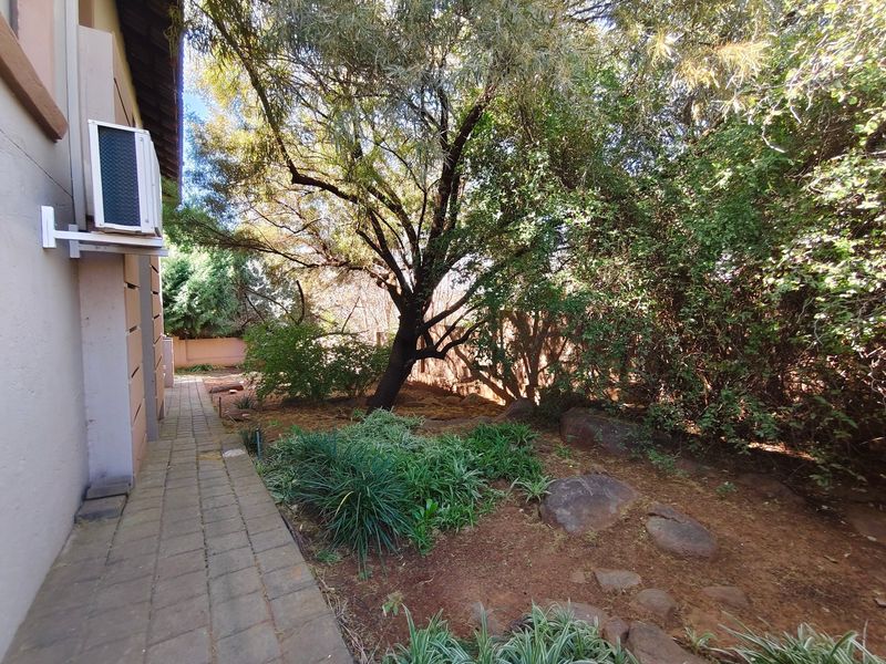 A side garden area featuring a paved walkway, established trees, and an exterior wall-mounted air conditioning unit.