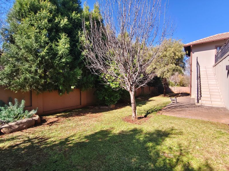 A private rear garden featuring a paved patio area, established trees, and an external staircase leading to the upper level of the house.