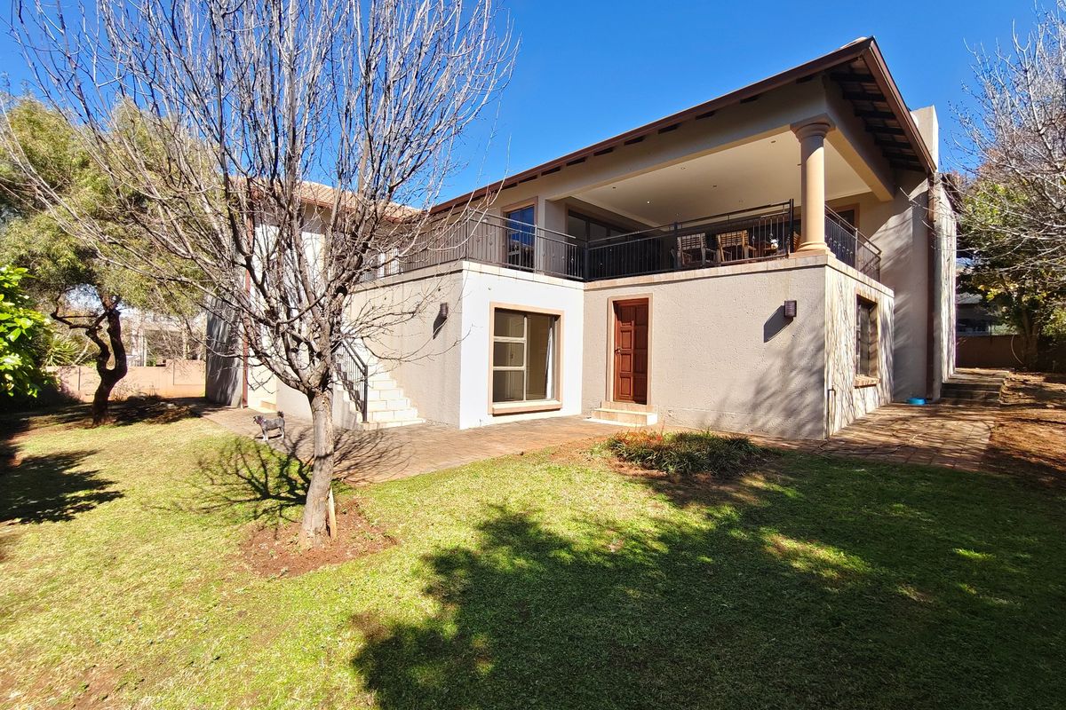 Rear view of the house featuring a spacious covered patio, balcony with wrought iron railings, and a paved terrace overlooking the garden.