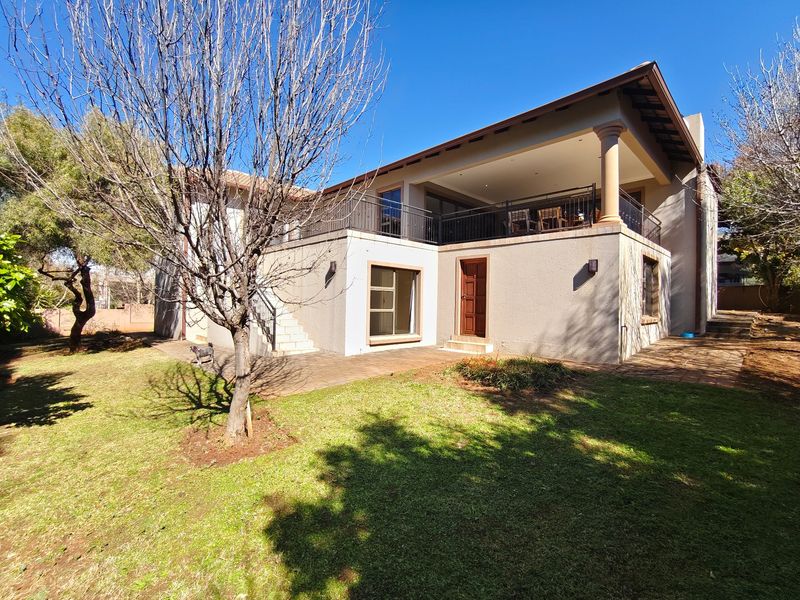 Rear view of the house featuring a spacious covered patio, balcony with wrought iron railings, and a paved terrace overlooking the garden.