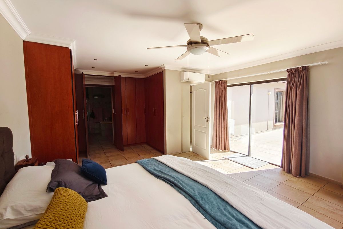 Spacious bedroom featuring built-in cupboards, tiled flooring, a ceiling fan, and direct access to an outdoor patio area through sliding glass doors.