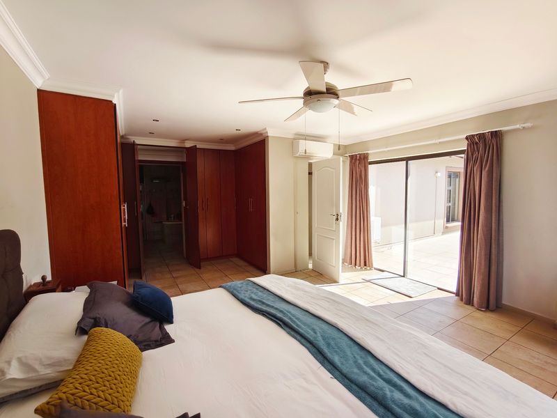 Spacious bedroom featuring built-in cupboards, tiled flooring, a ceiling fan, and direct access to an outdoor patio area through sliding glass doors.