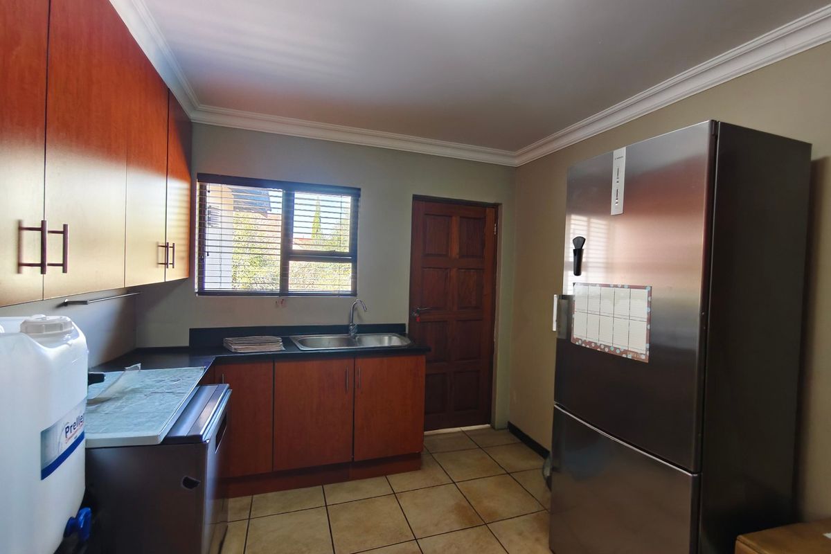 A functional kitchen featuring wood-finish cabinetry, laminate countertops, a stainless steel sink, and tiled flooring with coved cornicing.
