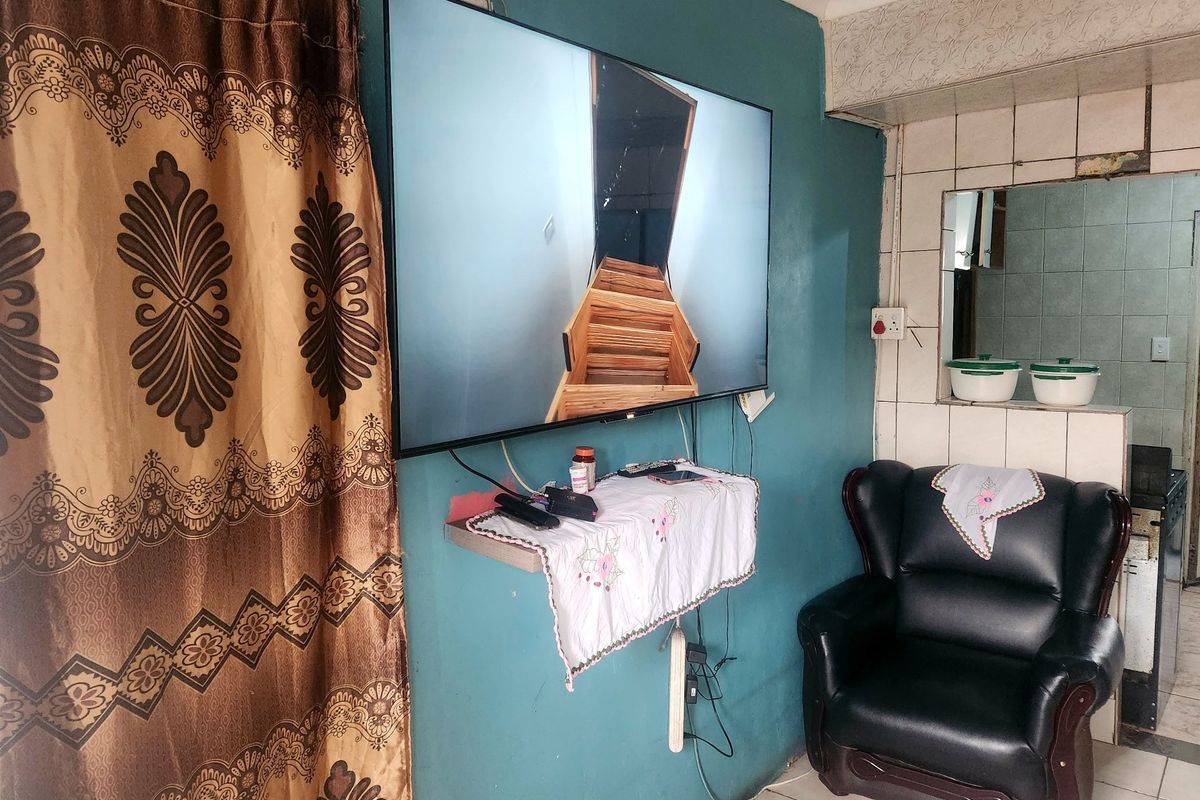 A living area featuring tiled flooring and a wall-mounted television, with a tiled partition wall separating the space from an adjacent area.