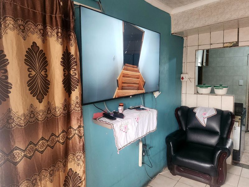 A living area featuring tiled flooring and a wall-mounted television, with a tiled partition wall separating the space from an adjacent area.