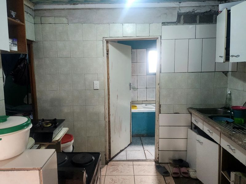 A dated kitchen area featuring tiled walls, cabinetry, and a stainless steel sink, requiring significant renovation and repair to improve functionality and aesthetics.