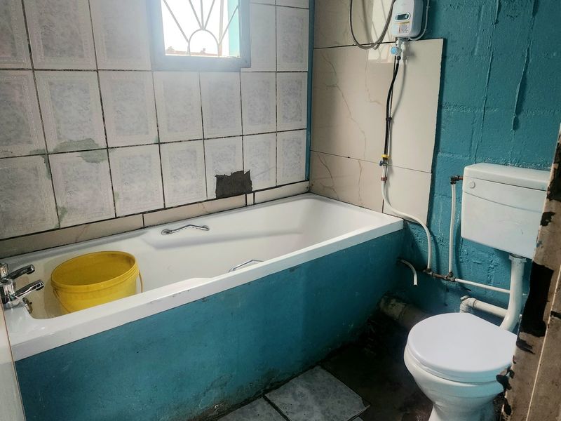 A dated bathroom featuring a bathtub, toilet, and electric shower unit, requiring significant renovation and cosmetic updates to improve its condition and functionality.