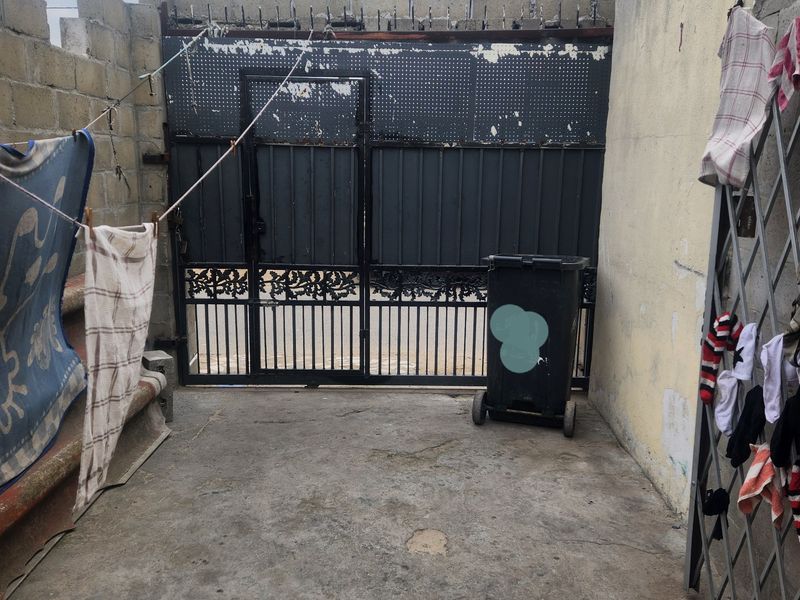 A gated entrance area featuring concrete block boundary walls and paved flooring, showing signs of significant weathering and wear.