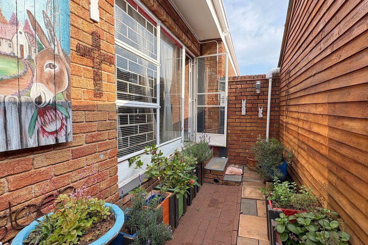 A narrow side courtyard featuring brick and timber wall finishes, a paved walkway, and secure window access.