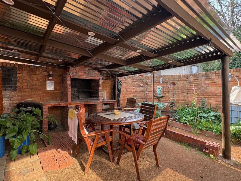 Covered outdoor patio area featuring a built-in brick braai, timber pergola structure with corrugated roofing, and brick boundary walls.
