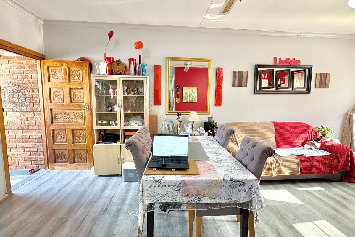 A living area featuring light-toned laminate flooring, a ceiling fan, and a decorative timber panel door leading to an exterior space.