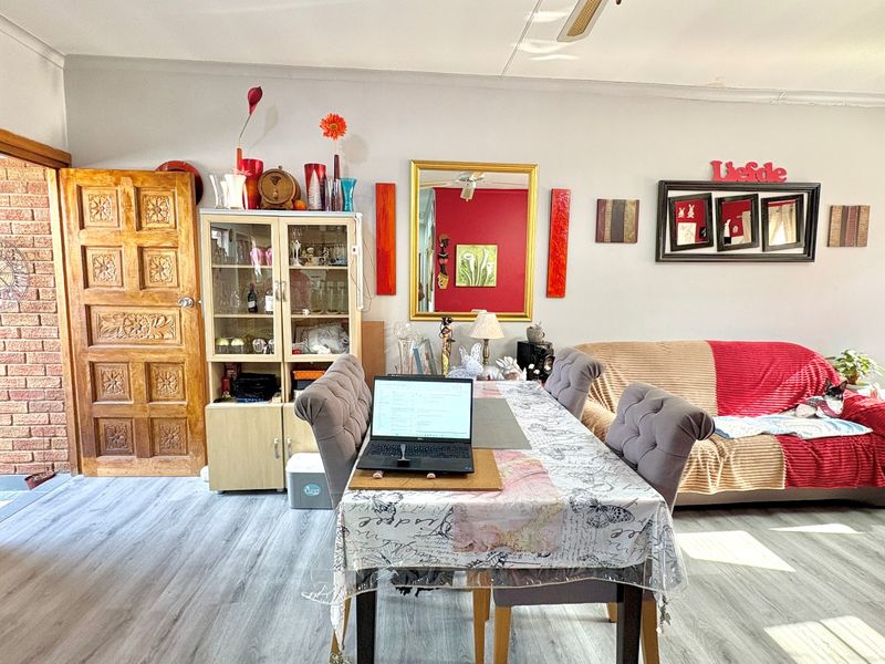 A living area featuring light-toned laminate flooring, a ceiling fan, and a decorative timber panel door leading to an exterior space.