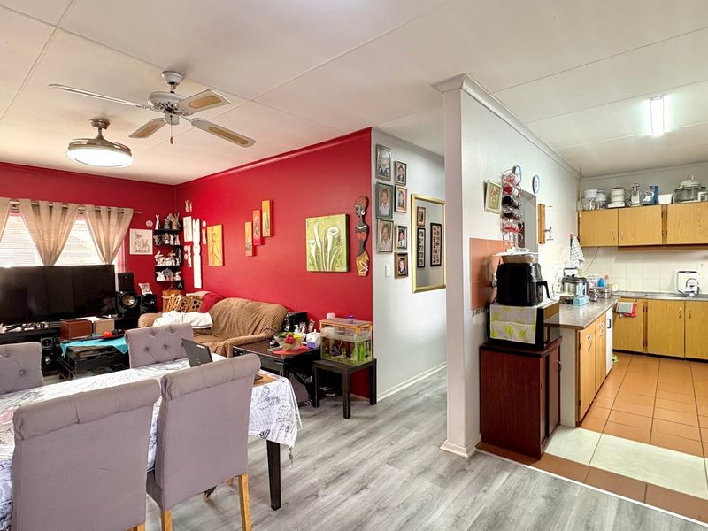 Open-plan living and dining area adjacent to a functional kitchen with wooden cabinetry and tiled flooring.