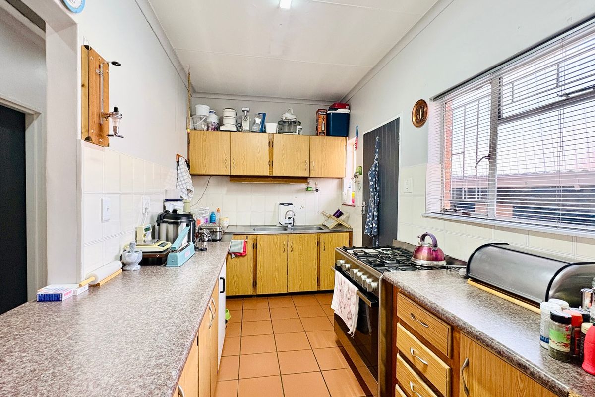 A functional kitchen featuring wooden cabinetry, laminate countertops, a gas stove, and tiled flooring, offering a practical layout with ample storage space.