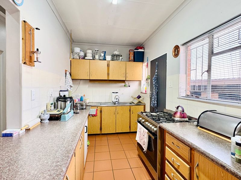 A functional kitchen featuring wooden cabinetry, laminate countertops, a gas stove, and tiled flooring, offering a practical layout with ample storage space.