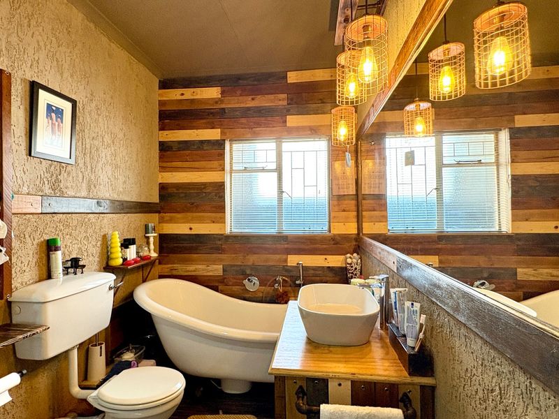 A rustic-style bathroom featuring a freestanding bathtub, vessel sink on a timber vanity, and distinctive textured walls with wood paneling accents.
