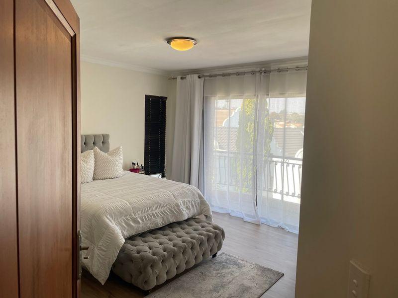 A well-lit bedroom featuring laminate flooring, a ceiling light fixture, and a sliding glass door providing access to a private balcony.
