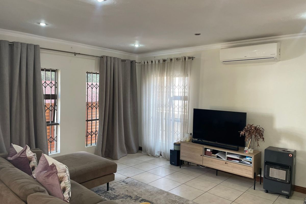 A well-maintained living room featuring tiled floors, recessed downlighting, and a wall-mounted split-system air conditioner for climate control.