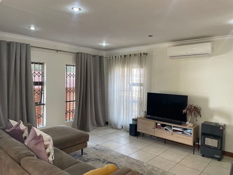 A well-maintained living room featuring tiled floors, recessed downlighting, and a wall-mounted split-system air conditioner for climate control.