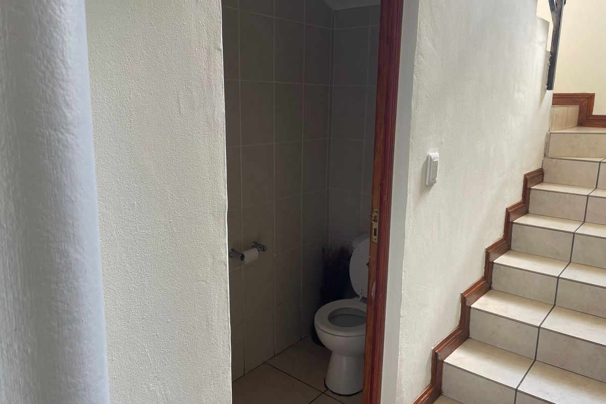 A compact guest bathroom located under the staircase, featuring tiled finishes and a standard toilet.