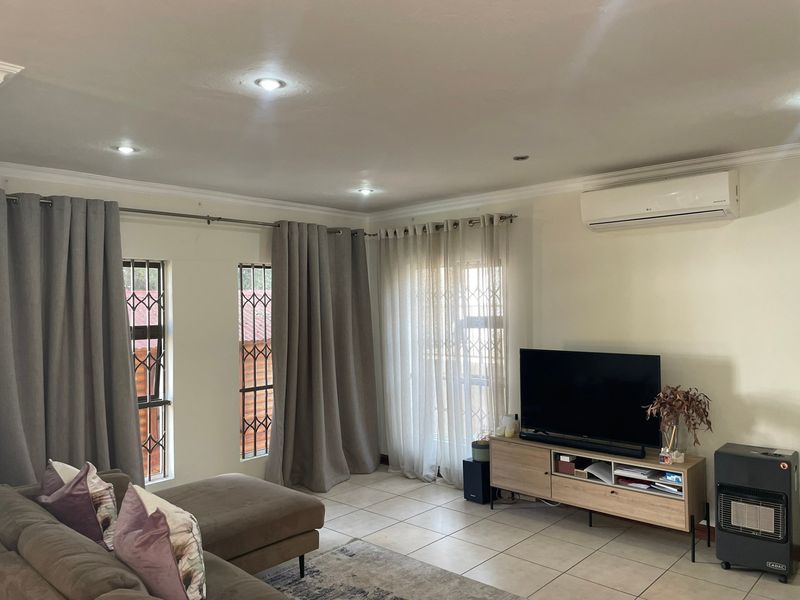 A well-lit living room featuring tiled floors, recessed ceiling lights, and a wall-mounted air conditioning unit.