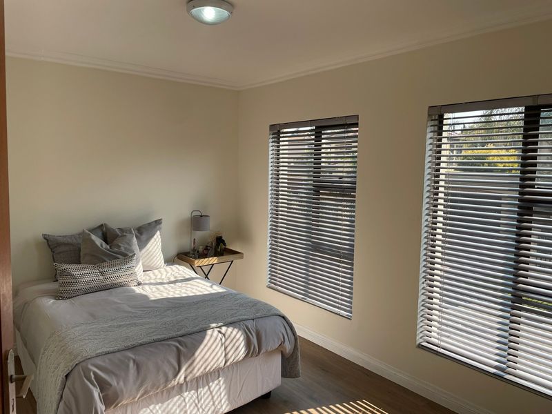 A bright and well-maintained bedroom featuring laminate flooring, neutral walls, and dual windows fitted with modern venetian blinds.