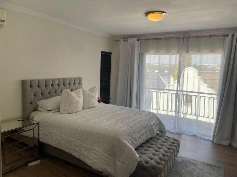 A well-maintained bedroom featuring laminate flooring, an air conditioning unit, and a sliding glass door that opens onto a private balcony.