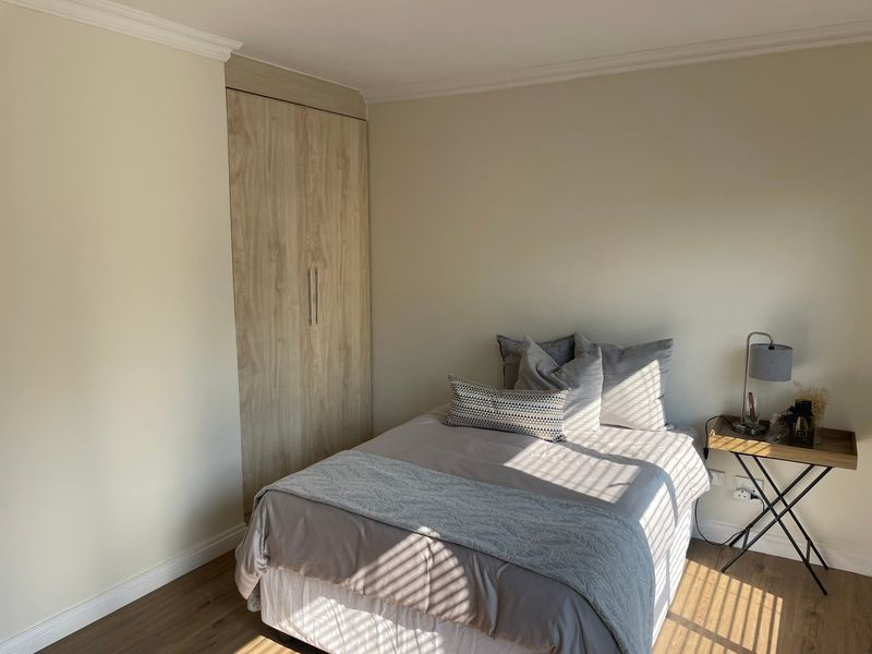 A well-maintained bedroom featuring neutral walls, laminate flooring, and a built-in wardrobe with a light wood finish.