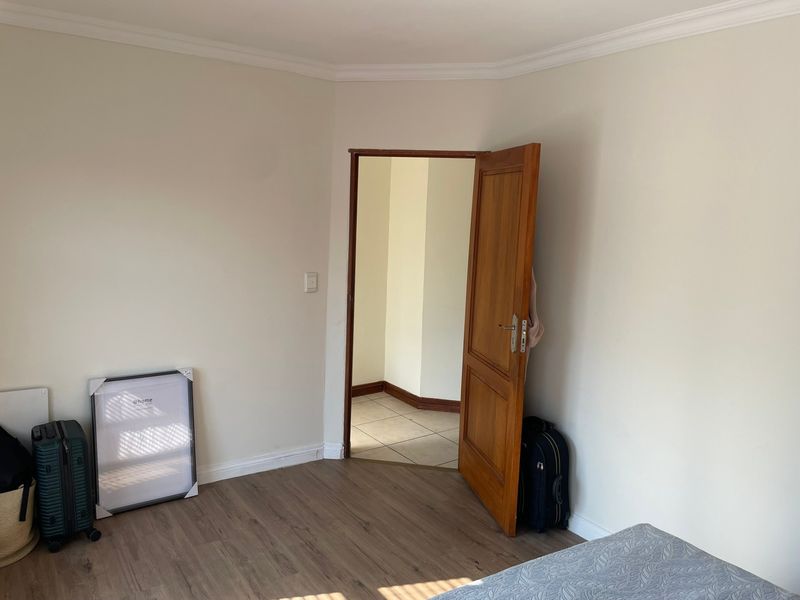 A clean, neutral bedroom featuring laminate flooring, coving, and a timber door leading to an adjacent tiled space.