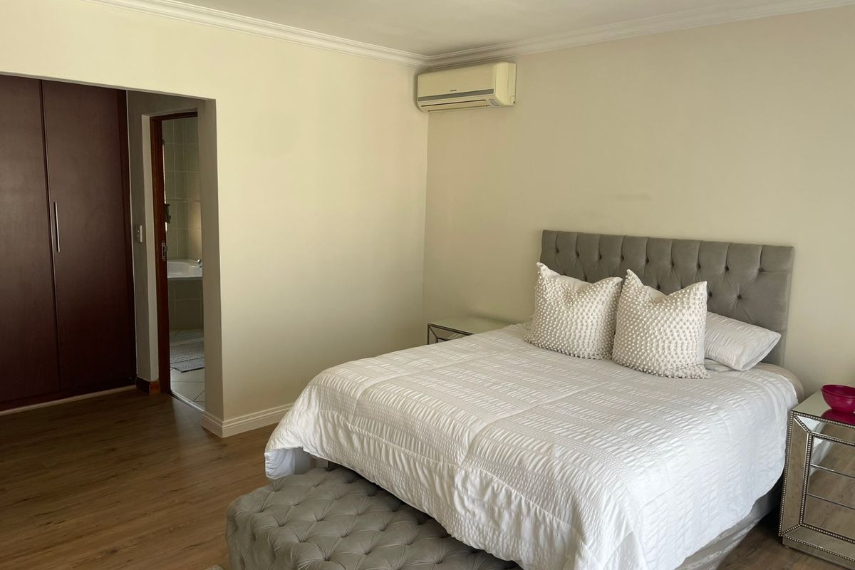 A well-maintained bedroom featuring laminate flooring, built-in cupboards, a split-system air conditioner, and direct access to an en-suite bathroom.