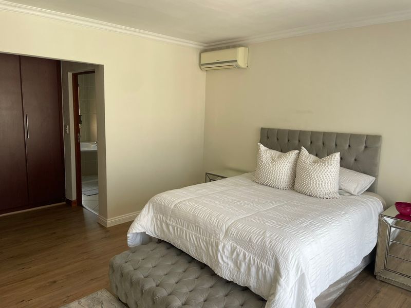 A well-maintained bedroom featuring laminate flooring, built-in cupboards, a split-system air conditioner, and direct access to an en-suite bathroom.