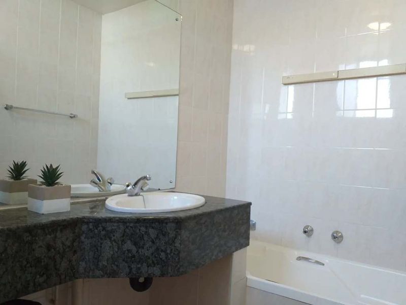 A functional bathroom featuring a granite vanity countertop, drop-in sink, and a built-in bathtub with tiled wall finishes.