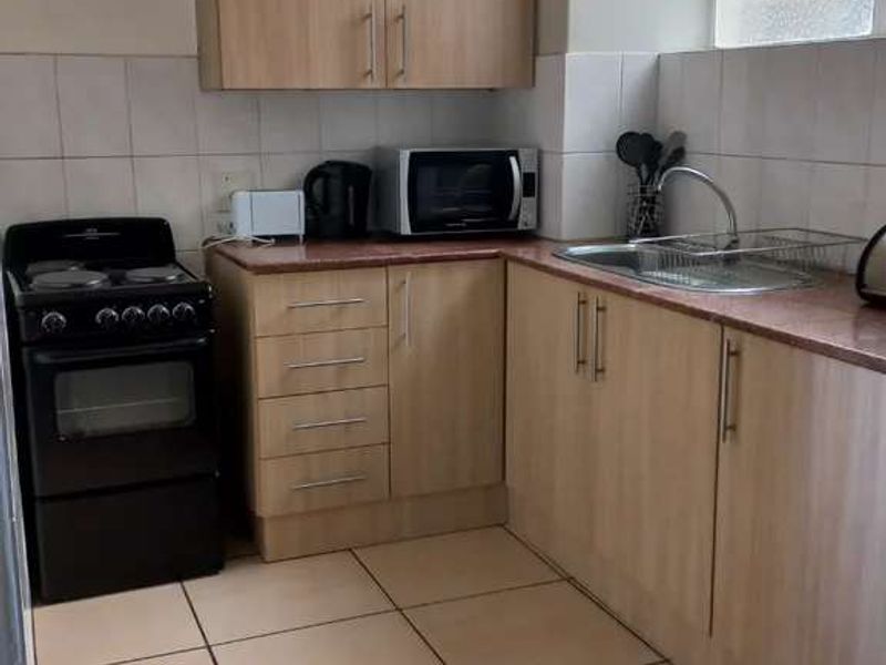 A functional kitchen featuring light wood-finish cabinetry, tiled flooring, a tiled backsplash, and a stainless steel sink with a freestanding stove.