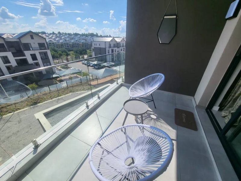 A modern apartment balcony featuring a sleek glass balustrade and tiled flooring, offering an elevated view of the surrounding residential complex.