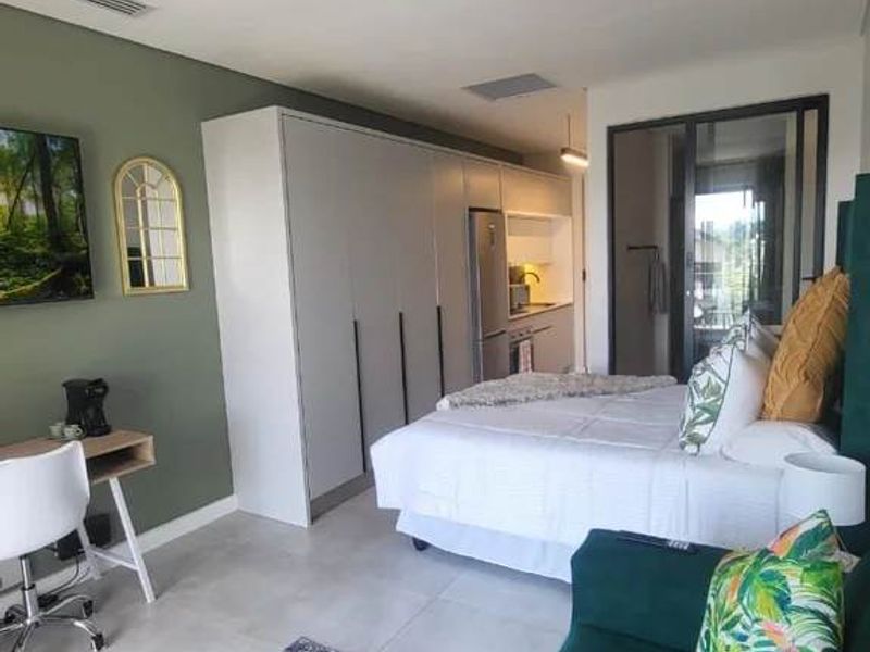 Modern open-plan studio apartment featuring sleek built-in cabinetry, tiled flooring, and seamless access to a private balcony through sliding glass doors.
