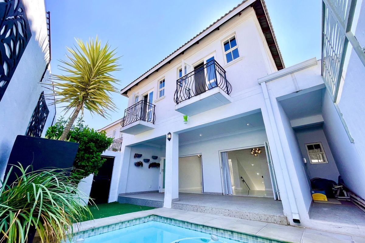 Rear exterior view featuring a swimming pool, covered patio area, and upper-level balconies with wrought iron railings.