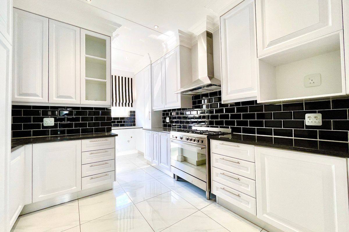 Modern kitchen featuring white shaker cabinetry, contrasting black subway tile backsplash, granite countertops, and high-end stainless steel appliances with polished marble-look flooring.