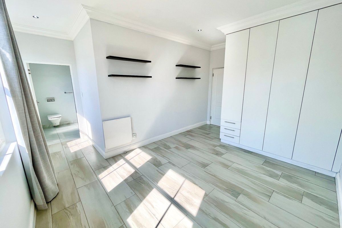 A bright, empty bedroom featuring modern tiled flooring, built-in cupboards, recessed lighting, and an en-suite bathroom access.