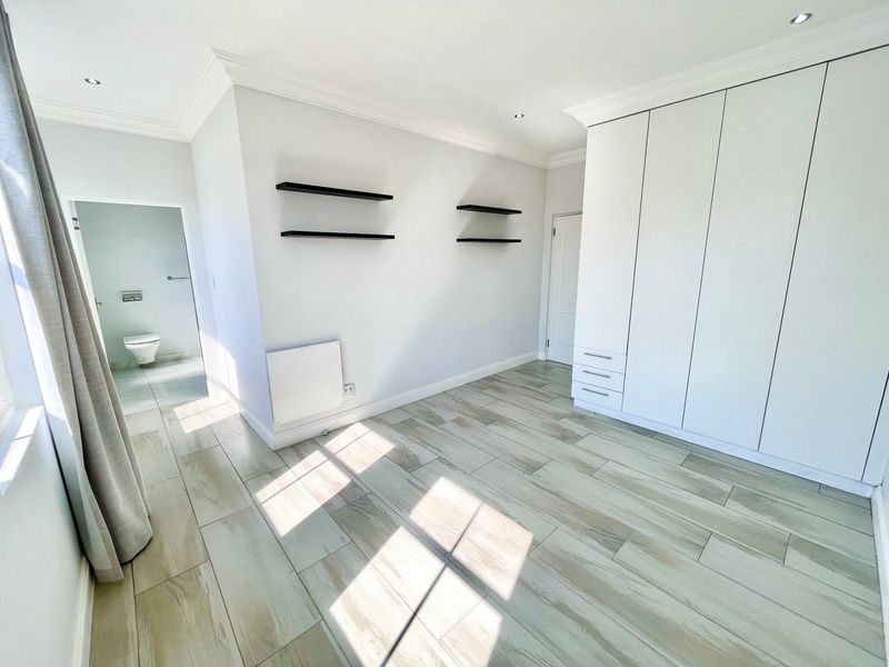 A bright, empty bedroom featuring modern tiled flooring, built-in cupboards, recessed lighting, and an en-suite bathroom access.