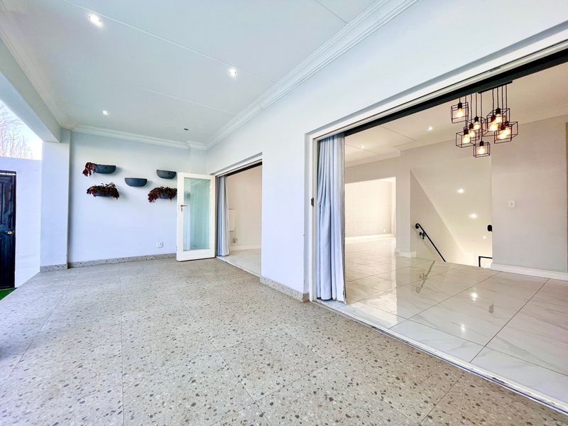 Spacious covered patio featuring terrazzo flooring and recessed lighting, providing seamless indoor-outdoor flow through large sliding glass doors to the interior living area.