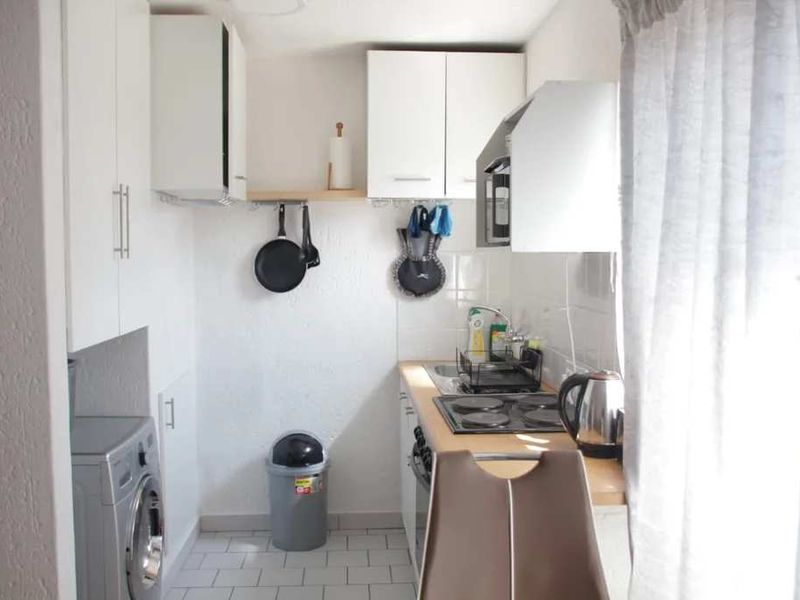 A compact, functional kitchen featuring white cabinetry, a built-in oven and hob, tiled backsplash, and integrated laundry appliance space.