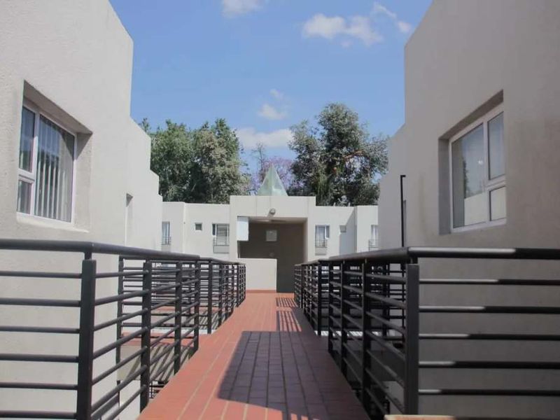 An elevated walkway with metal railings leading towards the apartment complex entrance, featuring tiled flooring and modern architectural design.