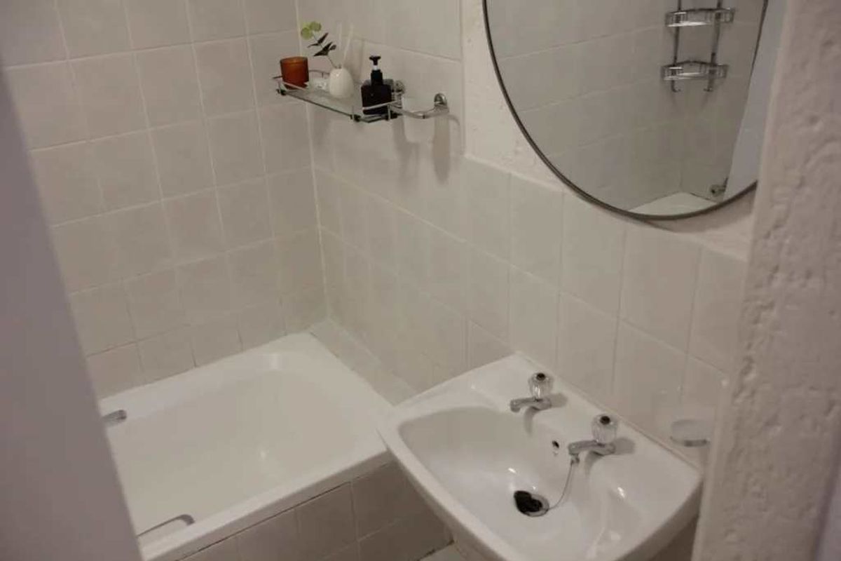 A functional bathroom featuring a white bathtub, pedestal basin, and wall-mounted mirror with neutral ceramic wall tiling.