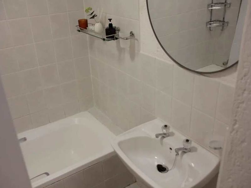 A functional bathroom featuring a white bathtub, pedestal basin, and wall-mounted mirror with neutral ceramic wall tiling.