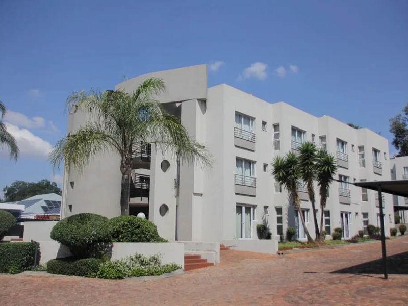 A multi-story apartment building featuring a paved driveway, covered parking, and landscaped garden areas.